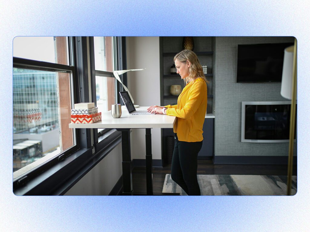A stylized stock photo of a woman at a standing desk, meant to demonstrate the benefits of asynchronous communication for WFH. 