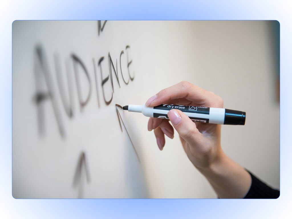 A stock photo of a person writing "AUDIENCE" on a whiteboard with arrows pointing to it. 
